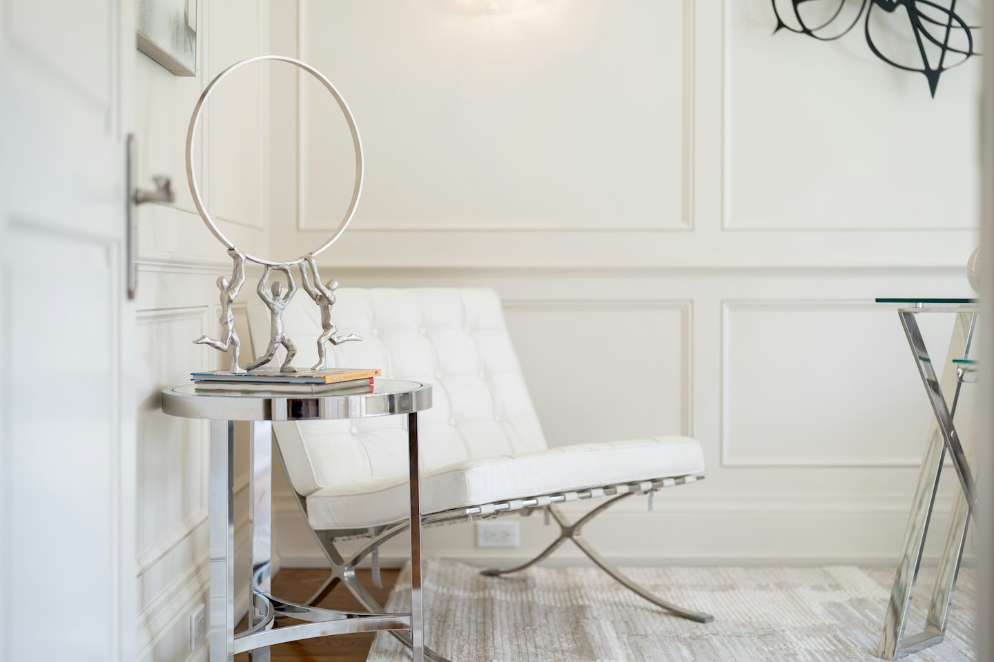 Silver sculpture rests on books beside a white leather armchair.