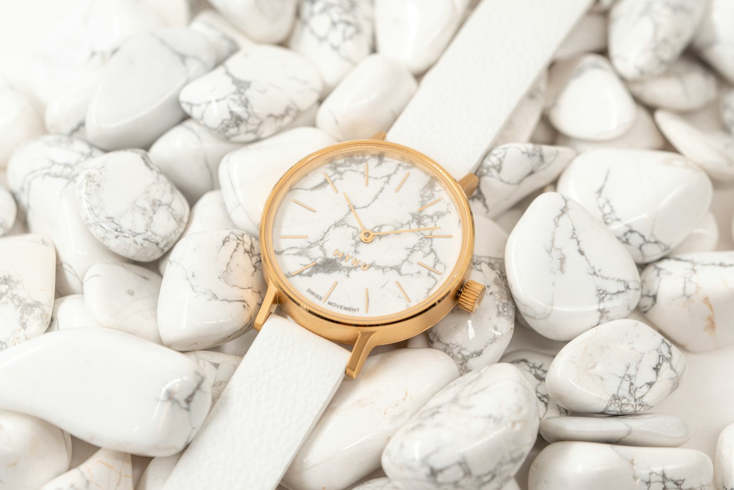A modern gold and white watch rests on marbled stones.