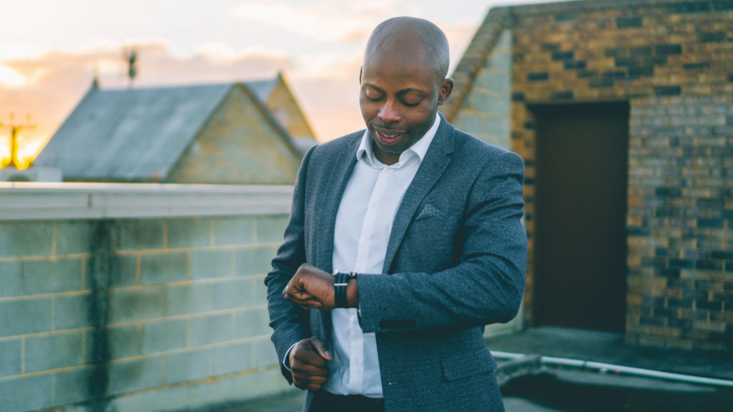 Man in suit checks smartwatch on urban rooftop at sunset.