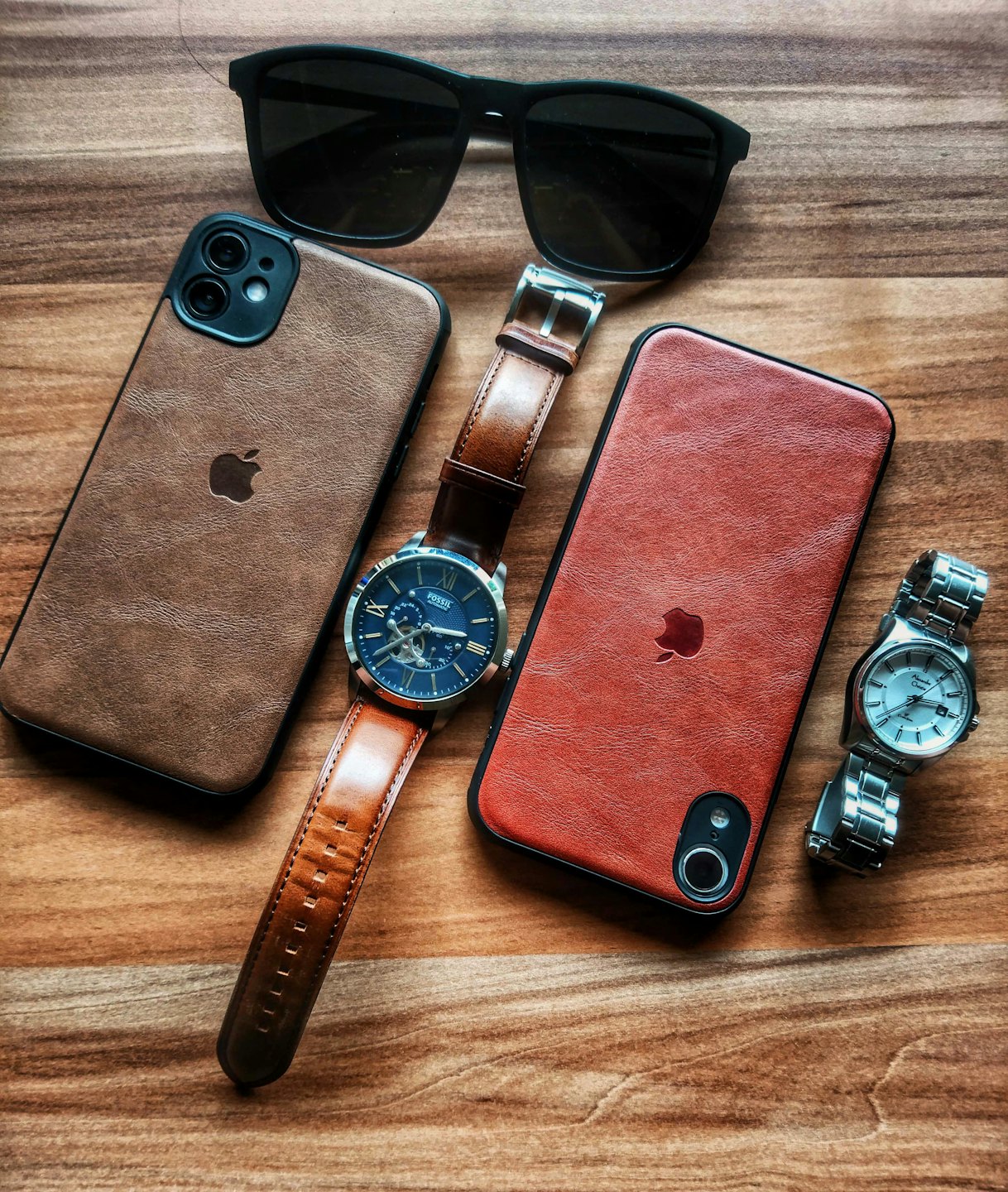 Two smartphones, two watches, and sunglasses arranged on wood.