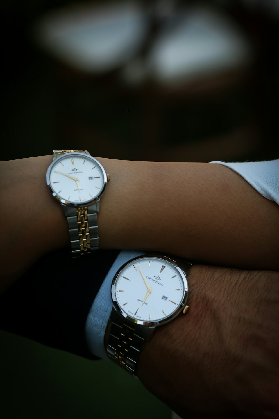 Two people display matching silver and gold wristwatches.